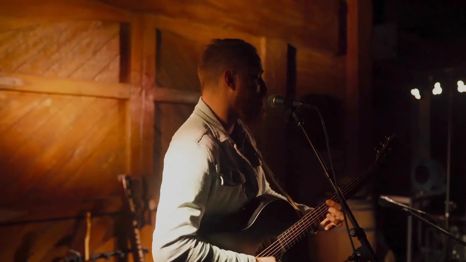 Roger Jæger singing with an acoustic guitar under warm stage light