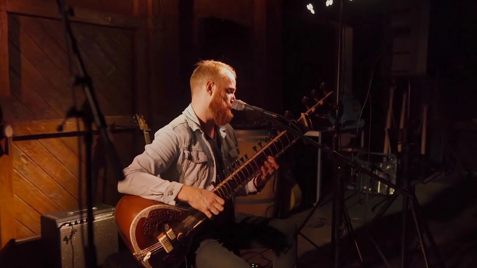 Roger Jæger playing sitar on stage in a wooden barn