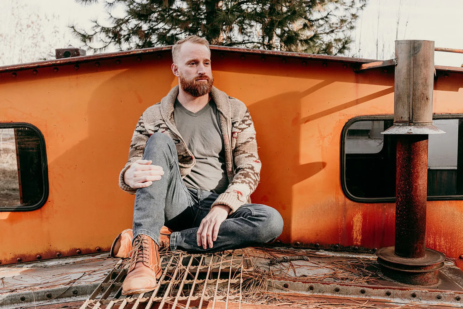 Roger sitting cross-legged on the deck of an orange caboose