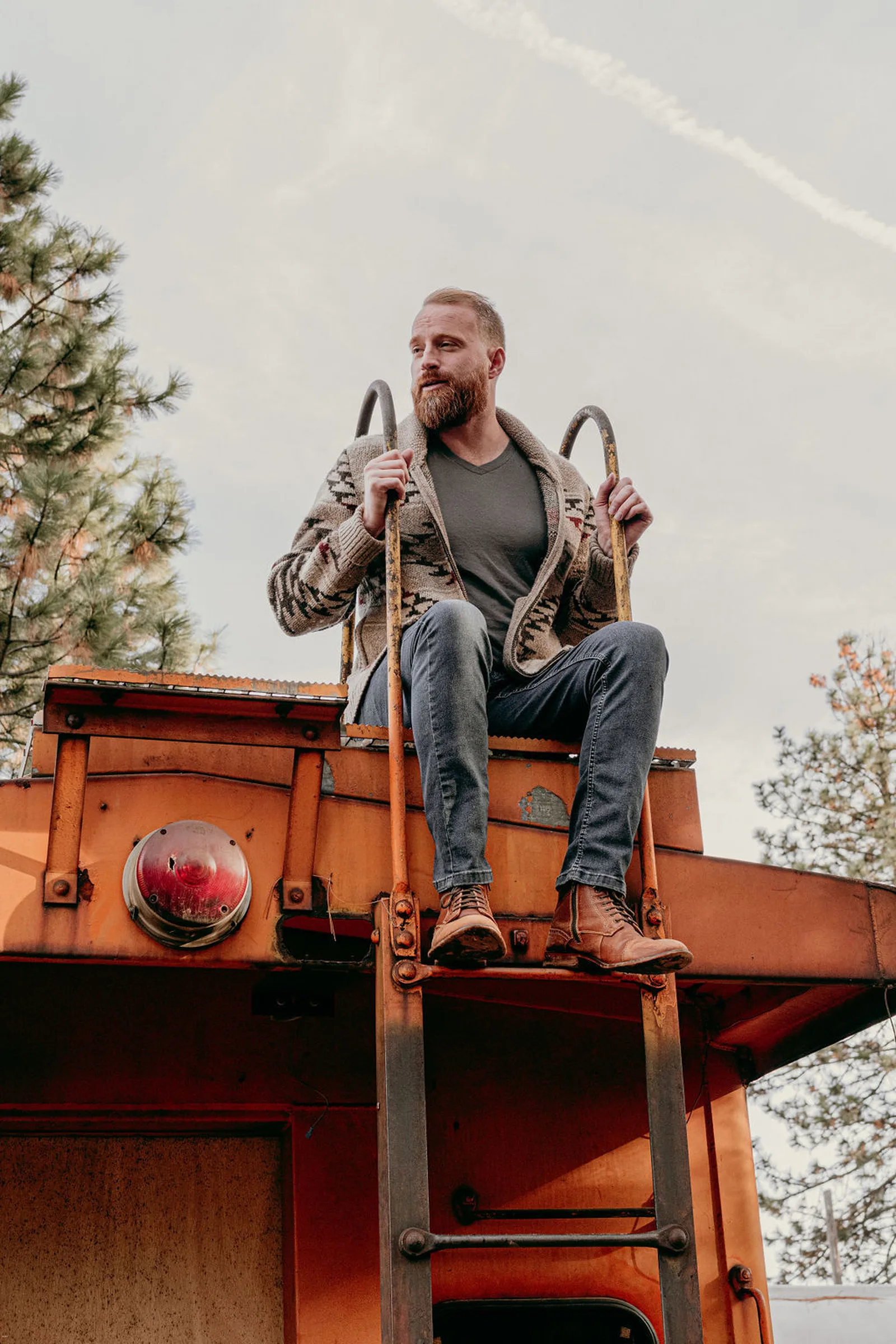 Roger sitting on the roof of an orange caboose against the sky