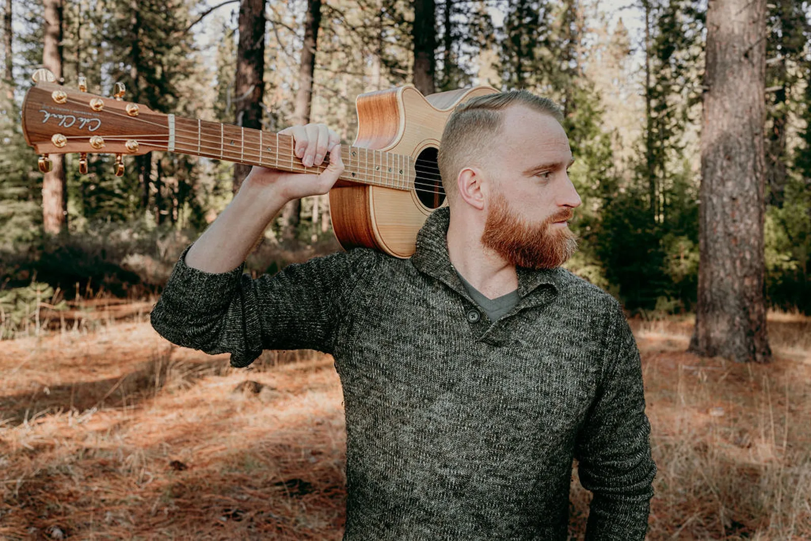 Roger with a Cole Clark guitar over his shoulder in the woods