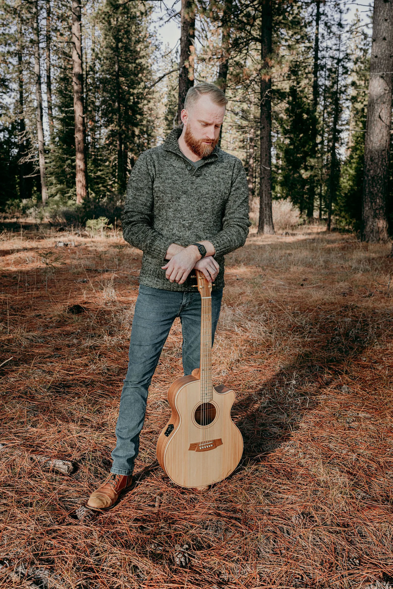 Roger standing in the pines, resting on his guitar